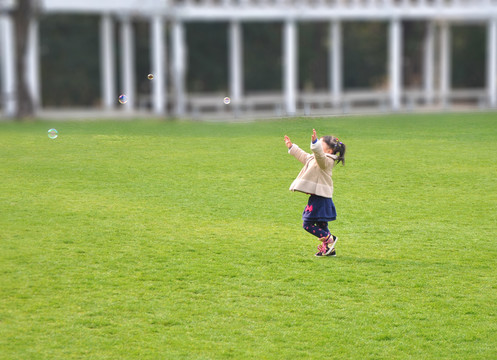 公园草坪上追逐肥皂泡的小女孩