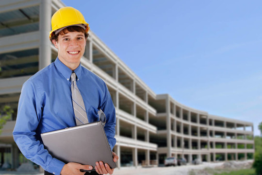 建筑工人手持筆記本電腦在商業(yè)建筑前