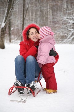 冬天，孩子親吻媽媽坐在公園雪橇里