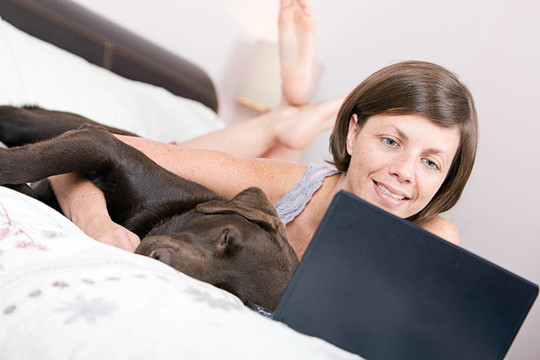 一個可愛的女人抱著她的拉布拉多犬在床上鏡頭而用自己的手提電腦