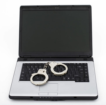 手铐在笔记本键盘。计算机/网络犯罪与网络成瘾概念。