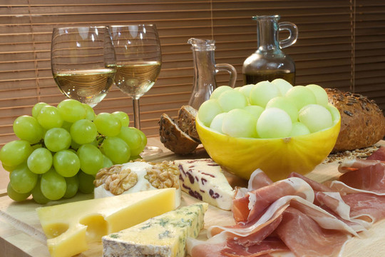一盤Mediterranean菜包括奶酪；葡萄；葡萄酒；面包；火腿；甜瓜；橄欖油和香醋。拍攝在美麗的