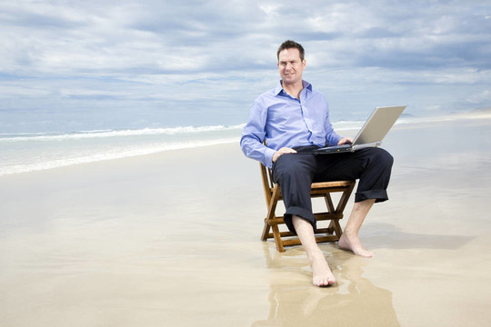 商务人士坐在海滩上的椅子上与笔记本电脑