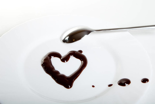 融化的黑巧克力在盘子和钢勺上。心的形状