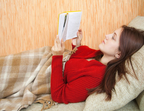 漂亮的年輕女孩在沙發(fā)上看書