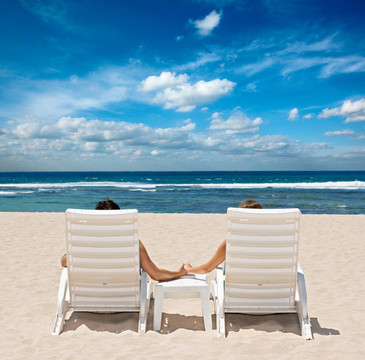 夫妇在海滩椅子手靠近海洋