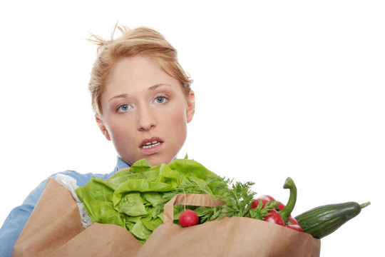 一個年輕的女人拿著一個食品袋，里面裝著新鮮健康的食品，白色背景