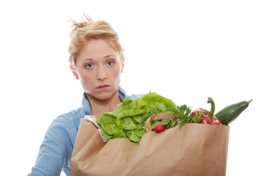 一個年輕的女人拿著一個食品袋，里面裝著新鮮健康的食品，白色背景