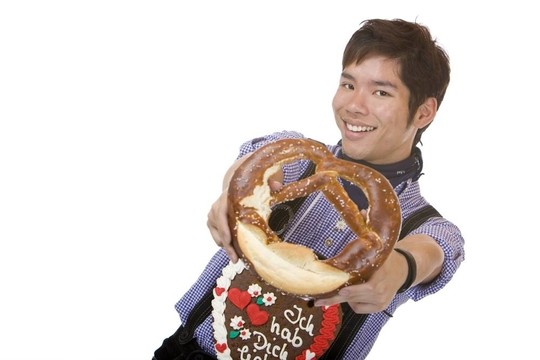 在Lederhose的亞裔男子在相機(jī)持有啤酒節(jié)餅干