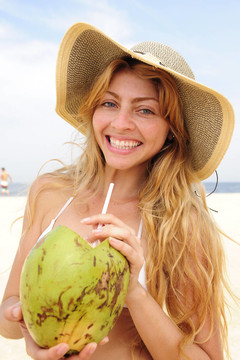 口渴的女人在海滩上喝椰子水