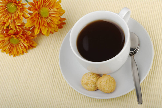 在帶茶托的茶杯紅茶；茶匙；餅干和背景中的橙花在杯墊（選擇重點）