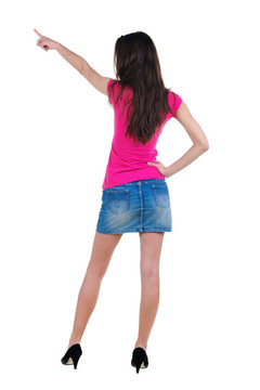 美麗的年輕女子在衣服指著墻壁。后視圖。