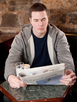 早上的咖啡和新聞-英俊的年輕人閱讀的報紙在BAE和喝咖啡