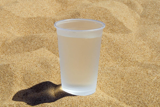 塑料玻璃與水站在沙灘上