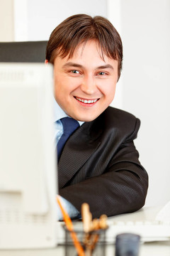 面带微笑的现代商人坐在办公桌前看着电脑显示器