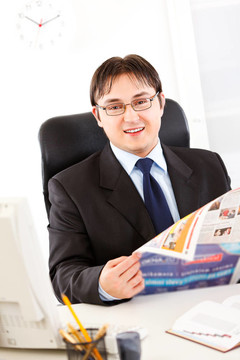 微笑的现代商人坐在办公桌前手里拿着报纸
