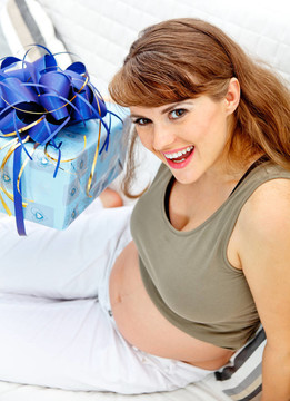 微笑美麗的孕婦坐在沙發(fā)上為她未出生的嬰兒