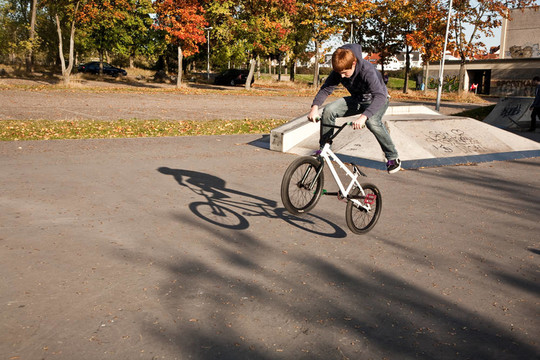 年輕的紅頭發(fā)的男孩是他的自行車(chē)在玩滑板公園跳