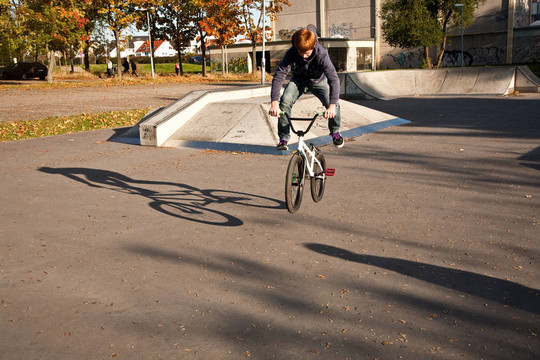 敬紅頭發(fā)的男孩是他的自行車在玩滑板公園跳