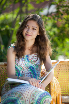 女孩讀的書坐在藤椅上在夏日戶外