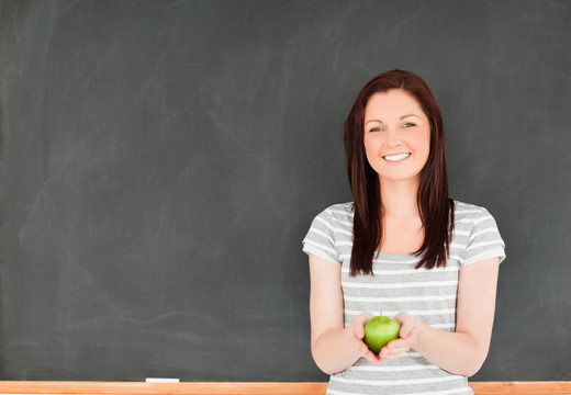 漂亮的年轻女子拿着一个苹果在黑板上