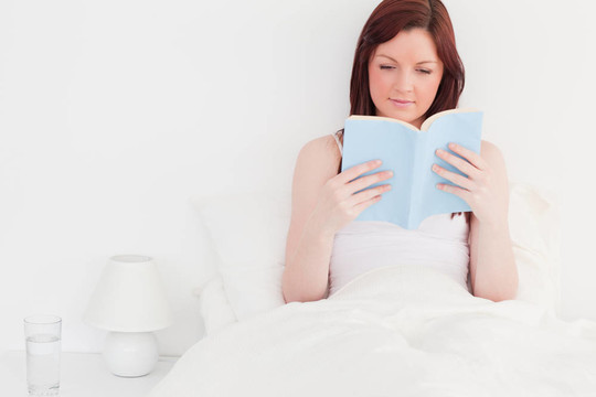 迷人的紅發(fā)女人坐在床上看書