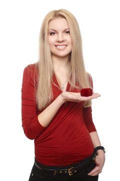 幸福的金發(fā)碧眼的年輕女子微笑著在紅色的衣服舉行一個(gè)紅色的盒子與戒指孤立的白色