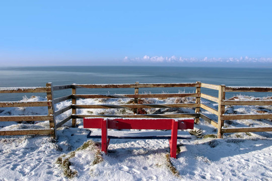 季節(jié)積雪覆蓋紅色長(zhǎng)凳海景