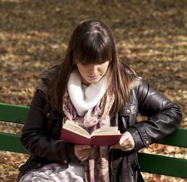美女坐在公園長椅上看書
