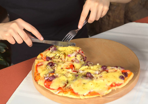 女人在家吃素食比萨（选择性焦点；焦点在手；餐具及餐具的披萨）