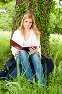 美丽的年轻女子在公园草地上看书