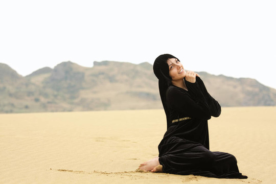 女人在披肩上坐在沙灘上仰望