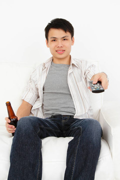 一個(gè)帶電視機(jī)遙控器和一瓶啤酒的亞洲年輕男子