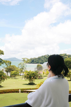 美麗的女士在陽臺(tái)上喝咖啡，擁有美麗的花園和海灘景觀