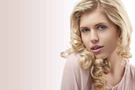新鮮和年輕漂亮的女孩穿著一件粉紅色的襯衣，卷曲的頭發(fā)在她的金色長發(fā)，美麗的臉看著相機(jī)與吸引人的姿勢對