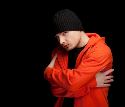 站在橙色的年輕人sweatshirtand黑帽；交叉雙臂；黑色背景