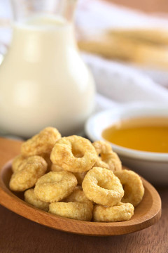蜂蜜味麥片圈后面有牛奶和蜂蜜的木勺子（選擇性聚焦；在前面上循環(huán)的前焦點(diǎn)）