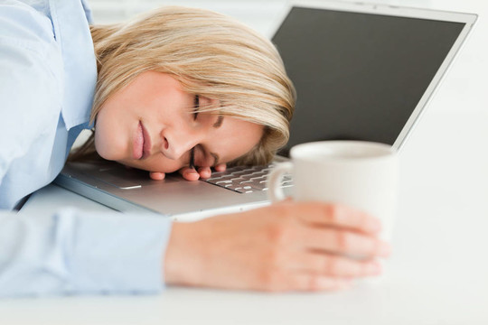 華麗的女人在她的筆記本電腦上睡覺，手里拿著一杯咖啡