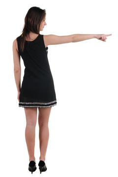 美麗的年輕女子在衣服指著墻壁。后視圖。