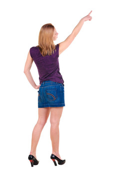 美麗的年輕女子在衣服指著墻壁。后視圖。