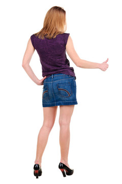 美麗的年輕女子在衣服指著墻壁。后視圖。