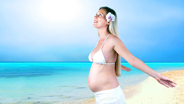 幸福的孕妇在阳光明媚的热带沙滩上