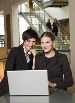 两个微笑的女商人在笔记本电脑前