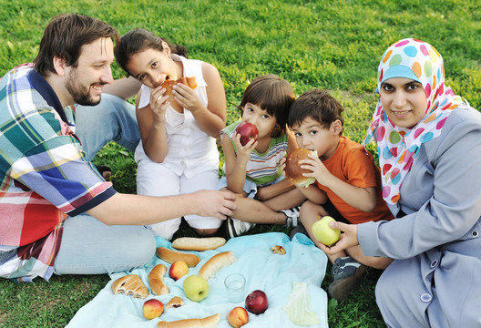 Muslim一家；母親和父親帶著三個孩子一起在大自然中坐著吃青草；野餐