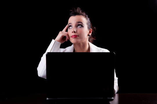 電腦上的漂亮女人；思考向上看；在黑色背景下孤立。工作室拍攝。