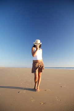 前戴帽子的女人在海灘上散步