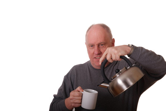 老年人在灰色的襯衫將熱水倒進杯茶凱特