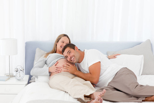 有趣的男人把頭放在懷孕妻子的肚子上