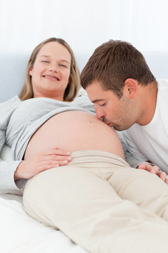 可愛的男人在床上親吻他懷孕的妻子的肚子