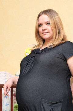 懷孕的年輕白人婦女站在嬰兒床旁邊。